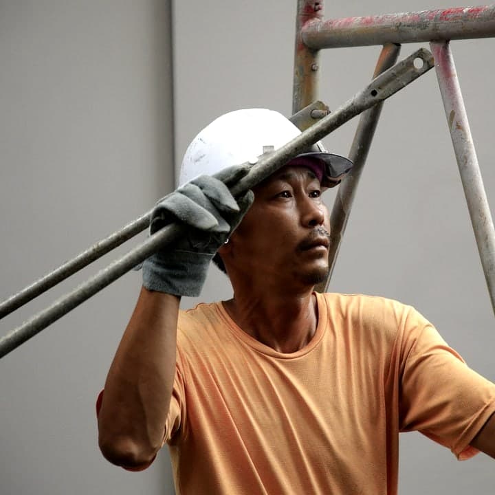 足場の管を握って見上げる職人